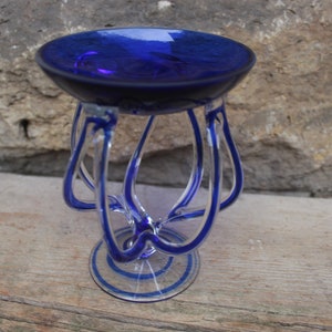 May include: A blue glass bowl with a clear glass stand. The stand has a unique design with multiple loops of glass.