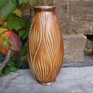 Könnte beinhalten: Eine hohe, braune Keramikvase mit einem strukturierten, blattartigen Design. Die Vase hat eine abgerundete, ovale Form und eine glänzende Oberfläche.