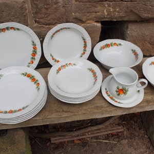 May include: A set of white porcelain dinnerware with a floral pattern featuring orange and green accents. The set includes plates, bowls, and a gravy boat.