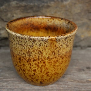 Puede incluir: Un pequeño cuenco de cerámica hecho a mano con una superficie moteada y texturizada. El cuenco presenta una cálida paleta de colores de tonos amarillo dorado y marrón. El borde tiene un patrón moteado más oscuro. Ideal para porciones pequeñas.