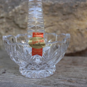 Op de afbeelding: Een heldere glazen kom met een geslepen kristallen ontwerp en een handvat. De kom heeft een label met de tekst "Anna Hutte Bleikristall 24% PbO Handarbeit Lead Crystal Crystal as Rock Tall Made in Germany".