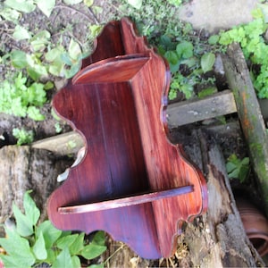 Könnte beinhalten: Ein Eckregal aus dunklem Holz mit einem dekorativen, gewellten Rand. Das Regal hat zwei Ebenen und ist in einem satten, rotbraunen Farbton gebeizt.