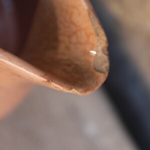 May include: Close-up of a chipped, light brown ceramic jug with a textured surface.