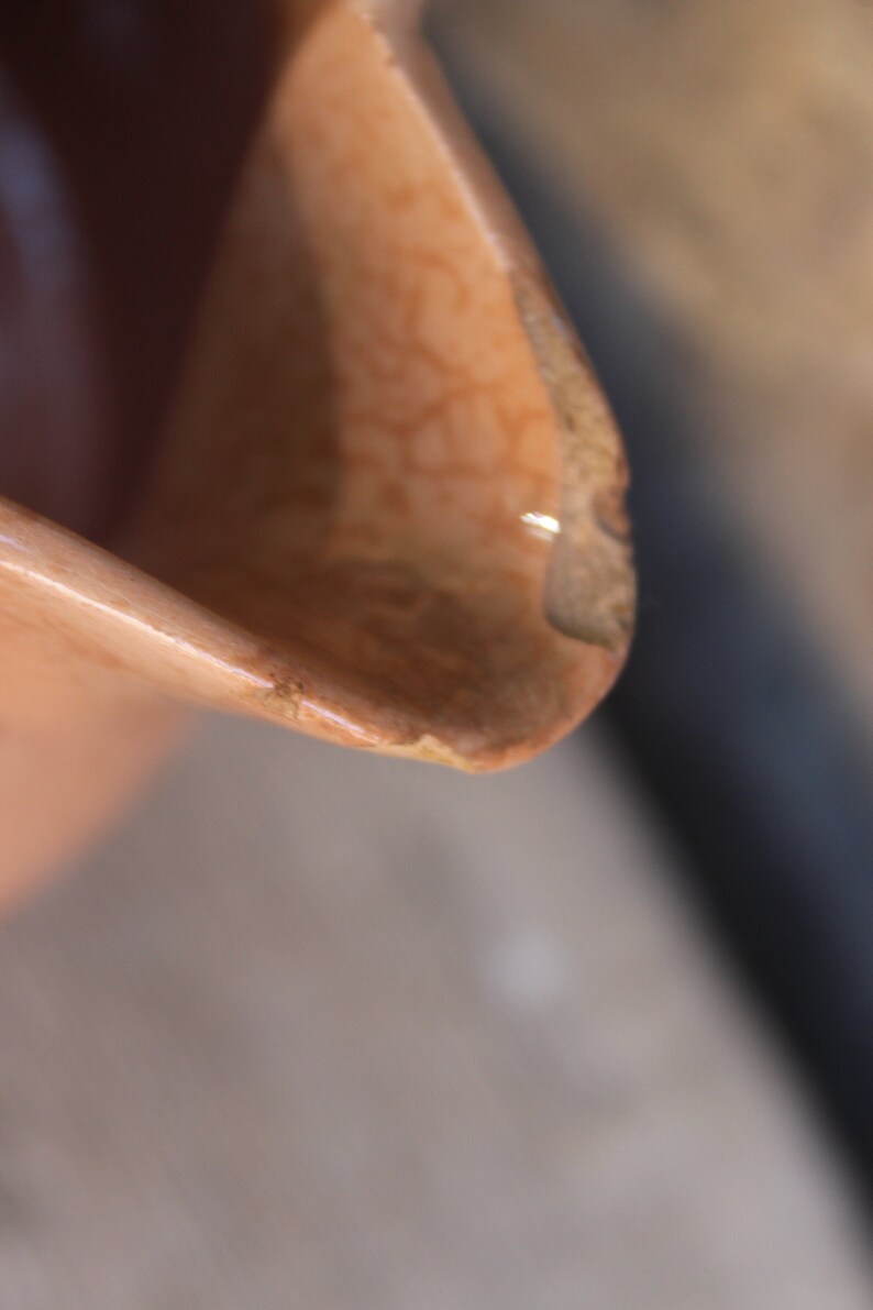 May include: Close-up of a chipped, light brown ceramic jug with a textured surface.