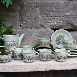 May include: A set of vintage floral teacups and saucers in a light green color with brown floral accents. The set includes a teapot, sugar bowl, and creamer.