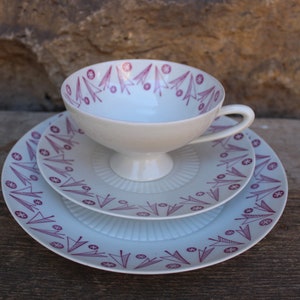 Peut inclure: Service à thé blanc avec une tasse, une soucoupe et une petite assiette assortie. L'ensemble présente un motif répétitif de formes géométriques magenta. La tasse repose sur un socle et les assiettes ont un design nervuré.