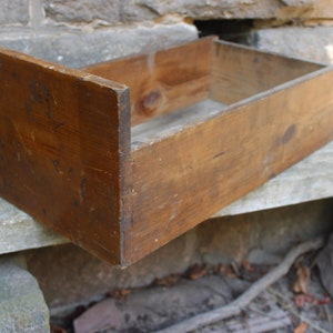 May include: A wooden drawer with a rustic brown finish. The drawer is empty and has a rectangular shape.