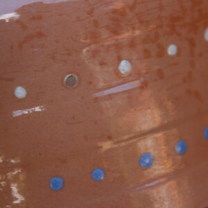 May include: A terracotta-coloured ceramic pot with a white and blue design. The pot has a textured surface and is decorated with white dots and blue circles.