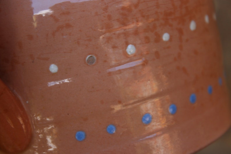 May include: A terracotta-coloured ceramic pot with a white and blue design. The pot has a textured surface and is decorated with white dots and blue circles.