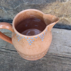 May include: A terracotta pitcher with a blue and white polka dot design. The pitcher has a handle and a wide mouth.