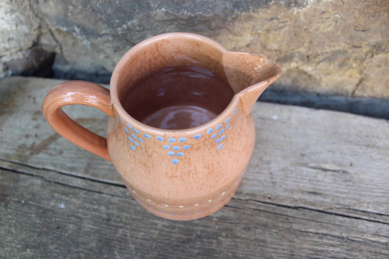 May include: A terracotta pitcher with a blue and white polka dot design. The pitcher has a handle and a wide mouth.