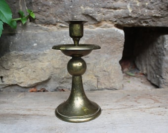 May include: A gold metal candlestick with a round base and a single candle holder.