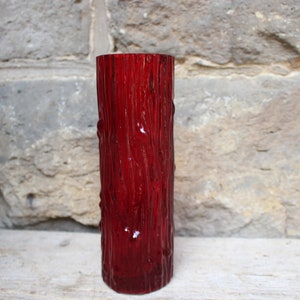 Può includere: Un vaso di vetro rosso con una texture a corteccia d'albero. Il vaso è cilindrico e ha una finitura liscia e lucida.
