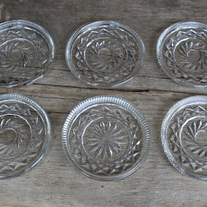 Può includere: Set di sei sottobicchieri in vetro trasparente con un design inciso decorativo. I sottobicchieri hanno un bordo rialzato e una forma circolare.