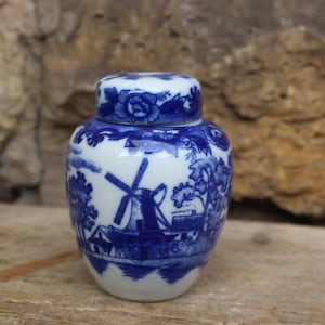 May include: A small blue and white porcelain jar with a lid. The jar is decorated with a windmill and a house in a landscape scene.