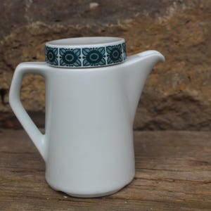 May include: White ceramic creamer with a green and white geometric pattern around the top.
