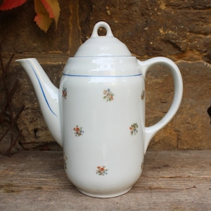 以下が含まれることがあります： 青い縁取りと花柄の白いセラミック製のコーヒーポット。ポットには蓋と取っ手があります。