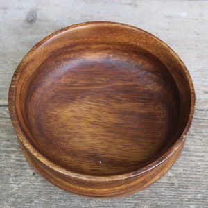 Puede incluir: Un cuenco redondo de madera, de color marr&oacute;n intenso y con veta visible. El cuenco tiene un dise&ntilde;o sencillo y cl&aacute;sico, ideal para servir alimentos o como elemento decorativo. Se encuentra sobre una superficie de madera envejecida.