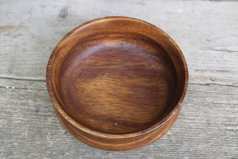 Puede incluir: Un cuenco redondo de madera, de color marr&oacute;n intenso y con veta visible. El cuenco tiene un dise&ntilde;o sencillo y cl&aacute;sico, ideal para servir alimentos o como elemento decorativo. Se encuentra sobre una superficie de madera envejecida.