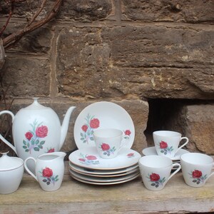 May include: A white tea set with a rose pattern. The set includes a teapot, sugar bowl, creamer, and four teacups and saucers.