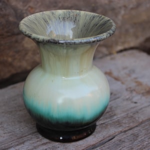 以下が含まれることがあります： 丸みを帯びたボディと広がった開口部を持つ小さなセラミックの花瓶。花瓶は緑、青、黒のグラデーションで釉薬がかけられています。