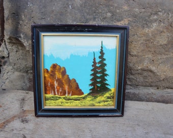 Könnte beinhalten: Ein gerahmtes Gemälde einer Landschaft mit blauem Himmel, grünen Bäumen und braunen Büschen. Das Gemälde ist in einem schwarzen Rahmen mit goldener Verzierung.