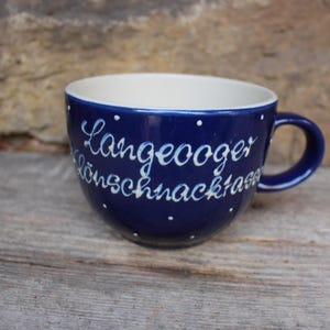 Puede incluir: Una taza de cerámica azul con lunares blancos y letras blancas que dicen "Langeooger Dönsschnackkraam".