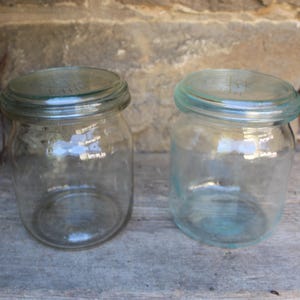 Op de afbeelding: Twee glazen potten met deksels. De potten zijn leeg en hebben een licht gematteerd uiterlijk.
