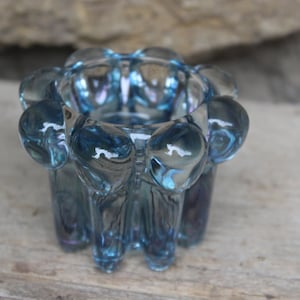 May include: A blue glass candle holder with a textured, bubble-like design. The holder has a round opening at the top and a wide base.