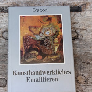 Könnte beinhalten: Ein graues Buch mit dem Titel "Brepohl Kunsthandwerkliches Emaillieren" und einem farbenfrohen abstrakten Gemälde auf dem Cover.