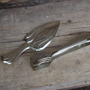 Peut inclure: Deux ustensiles de service en argent, l'un est un couteau à gâteau avec un motif décoratif et l'autre est une pince à sucre.