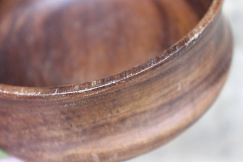 Puede incluir: Primer plano de un cuenco de madera con acabado marr&oacute;n oscuro. El borde del cuenco tiene un borde m&aacute;s claro y texturizado. La veta de la madera es visible, lo que se suma a la est&eacute;tica natural. La forma del cuenco es redonda y lisa.