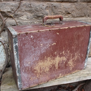 May include: A vintage wooden suitcase with a metal handle and metal trim. The suitcase is painted a dark red color and has a worn, distressed look.