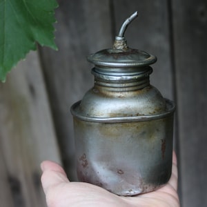 Peut inclure: Une vieille boîte à huile en métal avec un bec verseur et une finition argentée usée. La boîte est légèrement bosselée et présente des traces de rouille.