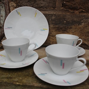 May include: Set of four white teacups and saucers with a geometric pattern of colorful lines in blue, yellow, pink, and gray.