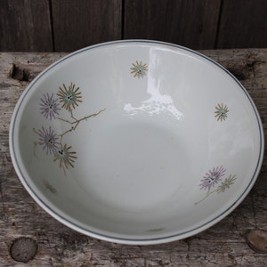 May include: A white ceramic bowl with a blue rim and a floral design featuring purple, green, and gold flowers.