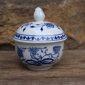 May include: A white porcelain sugar bowl with a blue and white floral design. The bowl has a lid with a knob on top.