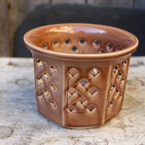 May include: A brown ceramic planter with a lattice design. The planter has a round top and a square base.