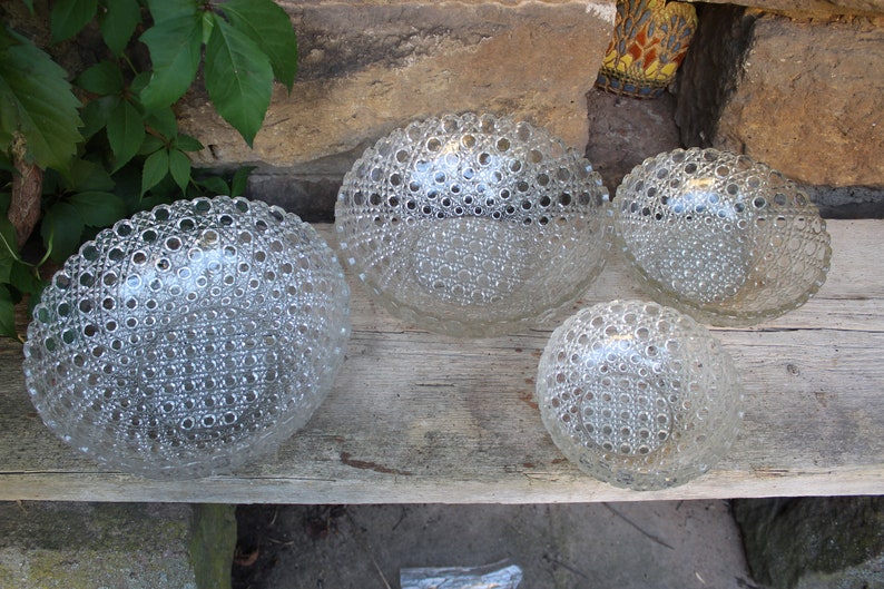 K&ouml;nnte beinhalten: Vier durchsichtige Glasschalen mit einem strukturierten, blasenartigen Design. Die Schalen sind in einer Reihe auf einer Holzoberfl&auml;che angeordnet.