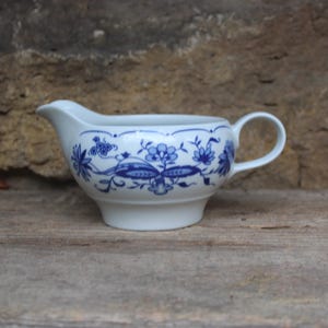 May include: A white porcelain gravy boat with a blue and white floral pattern. The boat has a rounded body and a handle on the right side.