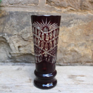 May include: A dark red glass vase with a cut glass design. The vase has a wide mouth and a narrow base.