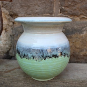 以下が含まれることがあります： 広口で丸みを帯びたボディのセラミック花瓶。花瓶は白、緑、黒のグラデーションで釉薬がかけられており、控えめなメタリックな光沢があります。