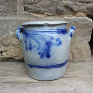 May include: A blue and white stoneware crock with two handles. The crock has a blue and white design on the front.