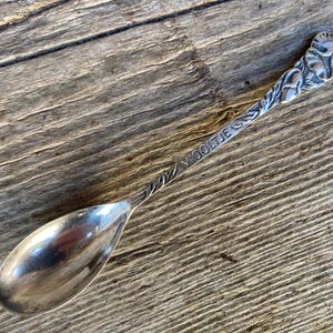 May include: A silver spoon with a floral handle and the word "VIOOLTJE" engraved on the stem. The spoon is displayed on a weathered wooden surface.
