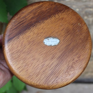 Puede incluir: Un cuenco redondo de madera, de color marr&oacute;n intenso con veta visible. El cuenco tiene una superficie lisa y pulida y una peque&ntilde;a etiqueta blanca en la base. El cuenco est&aacute; en la mano de una persona.