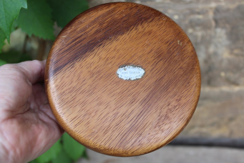 Puede incluir: Un cuenco redondo de madera, de color marr&oacute;n intenso con veta visible. El cuenco tiene una superficie lisa y pulida y una peque&ntilde;a etiqueta blanca en la base. El cuenco est&aacute; en la mano de una persona.
