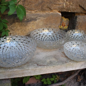 K&ouml;nnte beinhalten: Vier klare Glasschalen mit einem strukturierten Blasendesign. Die Schalen sind in einer Reihe auf einer Holzoberfl&auml;che angeordnet.