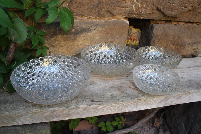 K&ouml;nnte beinhalten: Vier klare Glasschalen mit einem strukturierten Blasendesign. Die Schalen sind in einer Reihe auf einer Holzoberfl&auml;che angeordnet.