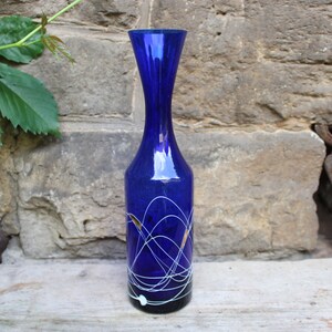 May include: A cobalt blue glass vase with a narrow neck and a wide base. The vase is decorated with white and gold swirling lines.