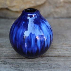 Könnte beinhalten: Eine kleine, runde blaue und weiße Keramikvase mit glänzender Oberfläche. Die Vase hat ein wirbelndes Muster aus Blau und Weiß.